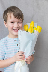A toddler smiling boy with a large bouquet of yellow tulips inMothers Day. Portrait of a happy little boy on a white background. Spring background