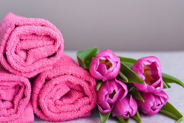 Obraz na płótnie Canvas a stack of pink towels in rolls with a bouquet of flowers, the concept of opening a new beauty salon and spa treatments