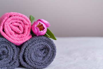 Obraz na płótnie Canvas a stack of fresh towels in rolls with a pink flower, the concept of housekeeping and laundry at the hotel