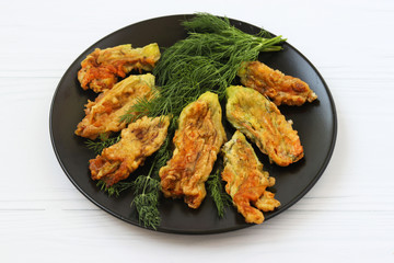 Fried zucchini flowers are located on a dark plate on a white background, Top view