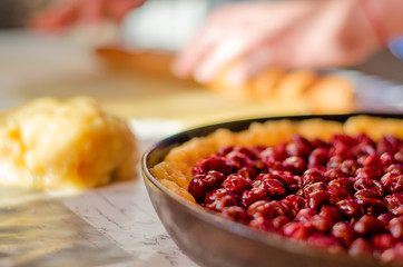The process of making cherry pie. Close- up of an UN-baked pie in a baking dish , with cherry berries piled on top. Selective focus, background blur.