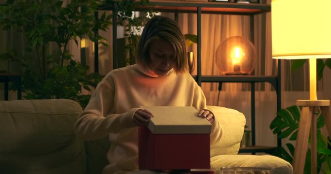 Woman surprised on opening gift box sitting on sofa at night