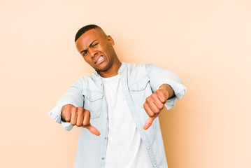 Fototapeta premium Young latin man isolated on beige background showing thumb down and expressing dislike.