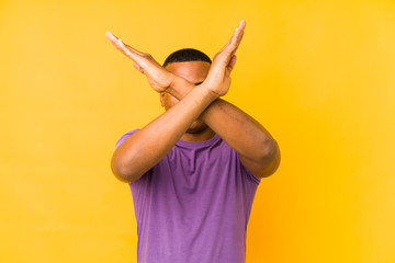 Young latin man isolated on yellow background keeping two arms crossed, denial concept.
