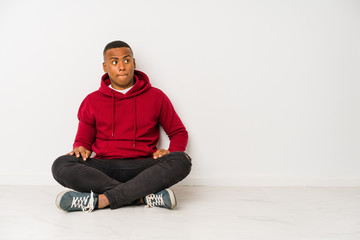 Young latin man sitting on the floor isolated confused, feels doubtful and unsure.