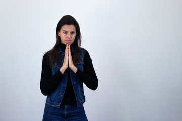 Portrait of attractive caucasian middle age woman model keeps palms together, praying, hopes for better and good luck, isolated on gray background studio shot, black sweater, denim jacket, jeans, dark