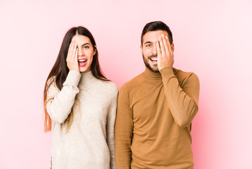 Young caucasian couple isolated having fun covering half of face with palm.