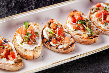Italian cuisine, antipasti and tapas. Bruschetta of baguette and cottage cheese, tomato, capers, pesto. Serving dishes in a restaurant in white plate. background image, copy space
