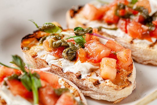 Italian cuisine, antipasti and tapas. Bruschetta of baguette and cottage cheese, tomato, capers, pesto. Serving dishes in a restaurant in white plate. background image, copy space