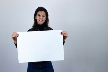 Portrait of happy pretty  middle age woman smiling holding a big white placard, sign Copy Space, isolated on gray background studio shot, dark air. Place for your text in copy space.