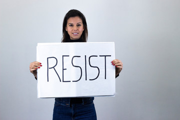 attractive  middle age woman activist hold up protesting sign saying "Resist" isolated on gray background studio shot, dark air. Place for your text in copy space.