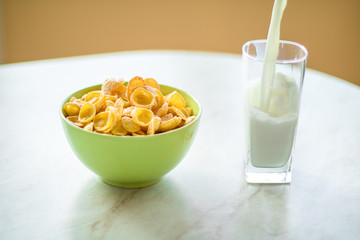 cornflakes in the green dish, milk is flowing into the glass