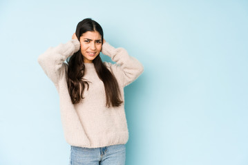 Young indian woman isolated on blue background covering ears with hands.