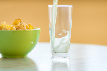 cornflakes in the green dish, milk is flowing into the glass