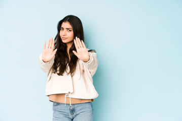 Young indian woman on blue background standing with outstretched hand showing stop sign, preventing you.