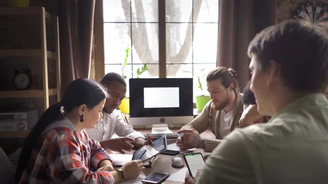 Innovative group of freelancers brainstorming ideas. Young afro american student or freelancer sitting at the table wth tablet pc and desktop pc. Showing his curator or coworker new project updates.