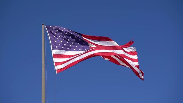 American Flag blowing in the wind with a blue sky background. USA American Flag. Waving United states of America famous flag in front of blue sky. Memorial Day - American concept.