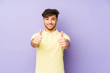 Young arabian man isolated on a purple background with thumbs ups, cheers about something, support and respect concept.