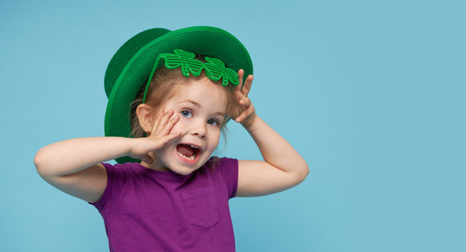 Funny little child girl in green Patricks hat with clover glasses on color background. St. Patricks Day celebration. Advertising space