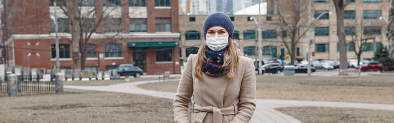 Caucasian mother in surgical mask walking with baby outdoor in Toronto. Protective face mask against Chinese pneumonia COVID-19 epidemic virus disease. Web banner header for a website.