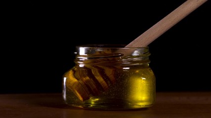 Honey dripping from honey dipper on black background. Healthy organic Thick honey dipping from the wooden honey spoon..