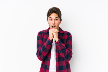 Young caucasian man posing in a pink background isolated praying for luck, amazed and opening mouth looking to front.