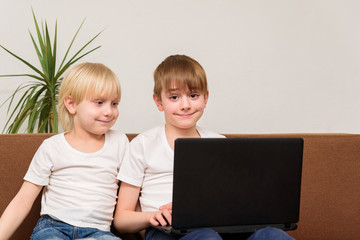 Two teenage boy sitting on sofa with laptop in hand and smiling.