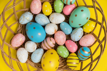 Closeup of Easter eggs in basket on yellow background. Multicolored festive eggs top view