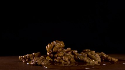 pour honey on walnuts which lie on a wooden board on a black background.