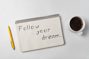 Notice motivational Follow your dream. Notepad, pen and cup of coffee on white background.
