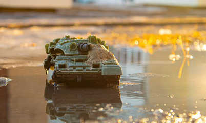 A small broken toy tank in a puddle in the sunset light.