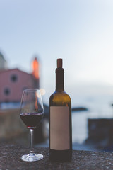 Bottle of wine with glass on the beautiful beach at the evening Italy. Wine is blurred. Sea and Lighthouse on the Background. Soft colours, Summer time. Copy Space For Text. Tellaro, Italy.