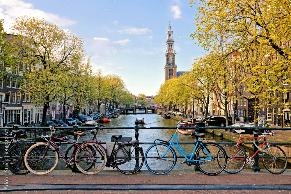 Wall mural Bicycles lining a bridge over the canals of Amsterdam with church in background. Late day light. Netherlands.