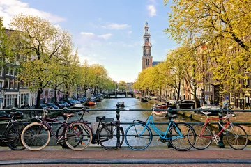 Poster de jardin Amsterdam Bicycles lining a bridge over the canals of Amsterdam with church in background. Late day light. Netherlands.