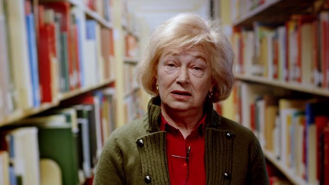 Blonde experienced librarian woman making a video talk online conversation training lecture or online course standing in library. Modern education. Job interview.