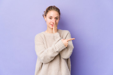 Young caucasian woman on purple background saying a gossip, pointing to side reporting something.