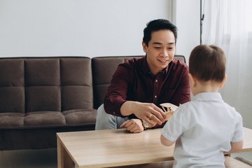 Obraz premium Asian dad and his cute little son playing with a wooden plane in a bright room