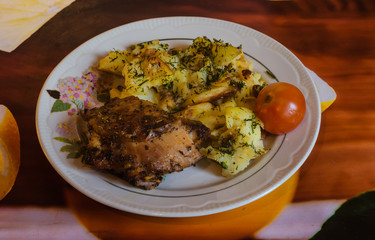 on a plate baked chicken meat with potatoes greens and tomato and