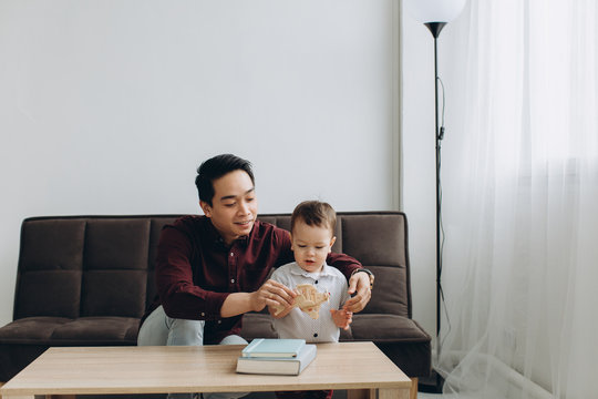 Asian Dad And His Cute Little Son Playing With A Wooden Plane In A Bright Room