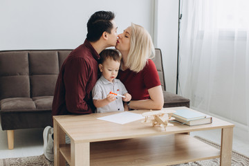 Happy multicultural family. Asian man and Caucasian woman drawing with their son.