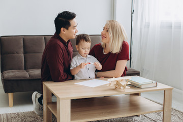 Fototapeta premium Happy multicultural family. Asian man and Caucasian woman drawing with their son.