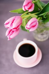 Fototapeta na wymiar Black coffee in a pink cup and pink spring tulips on a gray background. Top view