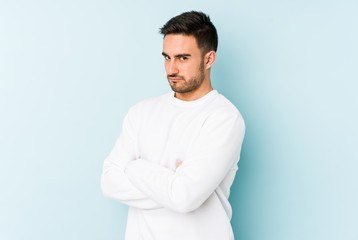 Young caucasian man isolated on blue background frowning face in displeasure, keeps arms folded.