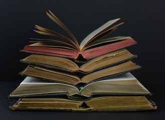 Old books with leather covers and red and gold yellow pages. Placed in pile on a dark background.