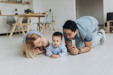 Happy multicultural family having fun together in the kitchen. Asian dad and caucasian mom teach son to crawl