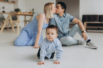 Happy multicultural family having fun together in the kitchen. Asian dad and caucasian mom teach son to crawl