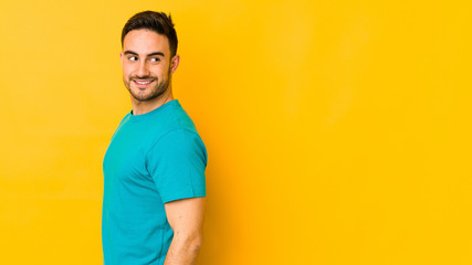 Young caucasian man isolated on yellow bakground looks aside smiling, cheerful and pleasant.