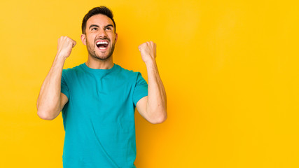 Fototapeta premium Young caucasian man isolated on yellow bakground raising fist after a victory, winner concept.