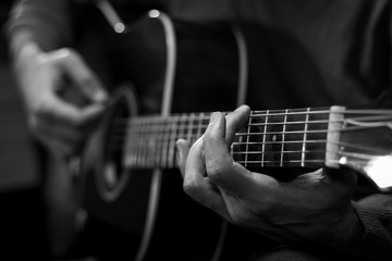 Fototapeta na wymiar Close up view of hands playing acoustic western guitar. Black and white image.