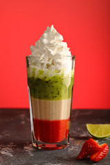 A multi-colored, delicious smoothie of strawberries, banana and kiwi fruit, with whipped cream, on a red background, a healthy and vitamin-rich drink made from fruits and berries.